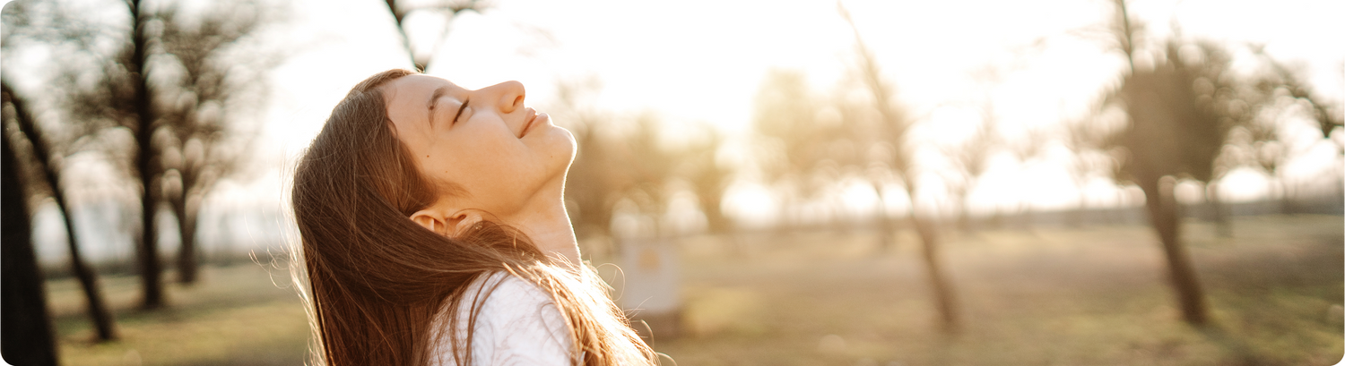 Woman with eyes closed in a park with blurred trees and sunlight